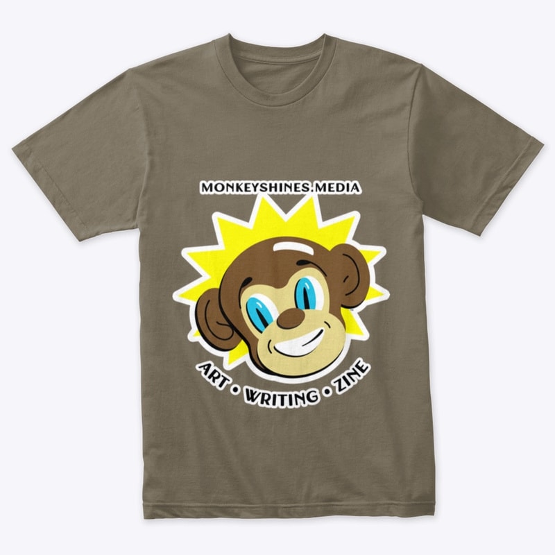A brownish-grey t-shirt with a color picture of the Monkeyshines mascot, Shiney the monkey, with the words 'monkeyshines.media' and 'art * writing * zine' in black around the picture.